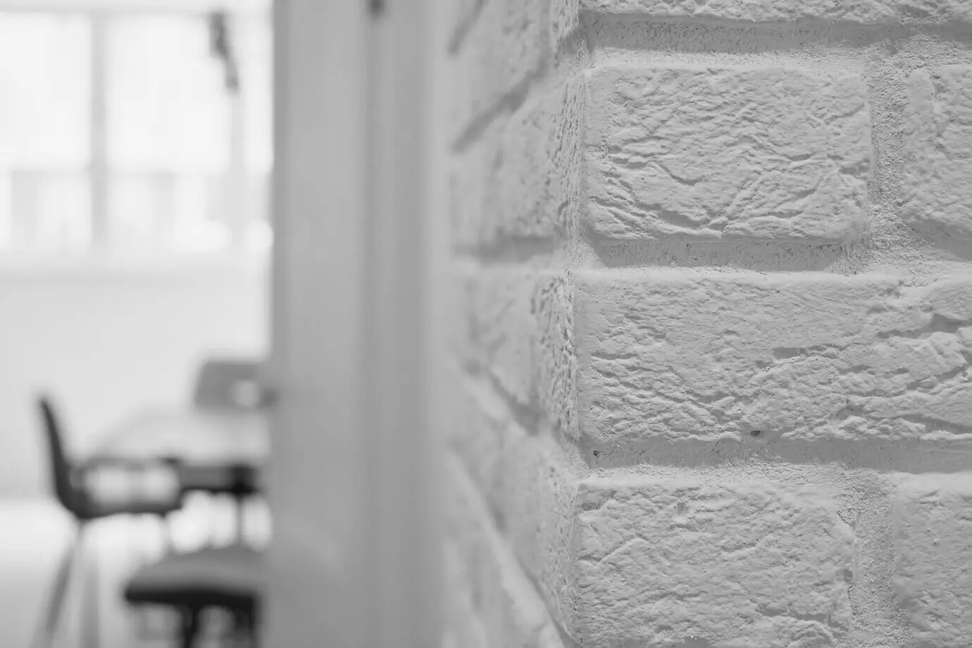 Schlichte Raumgestaltung mit weißer Ziegelwand und Möbeln vor unscharfem Raumhintergrund, Studio-Designidee im Loftstil, minimalistisches Design, angemessene Schlichtheit der Innenräume.